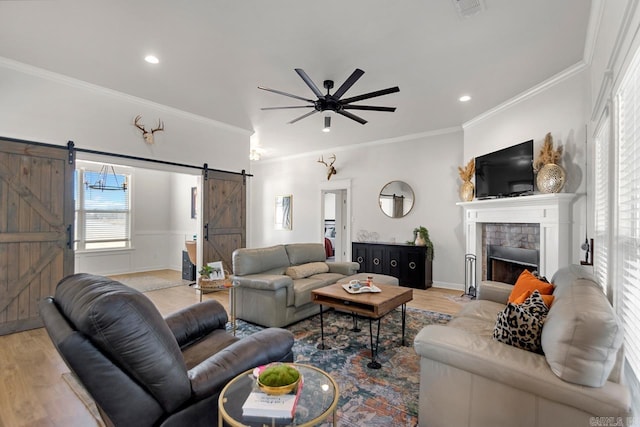 living room featuring a fireplace, crown molding, light wood finished floors, and a barn door