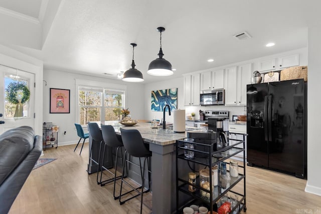 kitchen with light stone counters, stainless steel appliances, visible vents, white cabinetry, and a kitchen bar