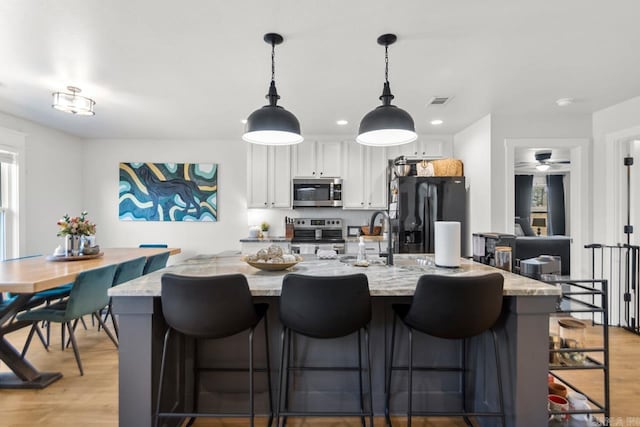 kitchen featuring white cabinets, light stone counters, a breakfast bar, hanging light fixtures, and stainless steel appliances