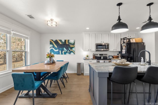 kitchen featuring hanging light fixtures, appliances with stainless steel finishes, white cabinetry, and light stone countertops