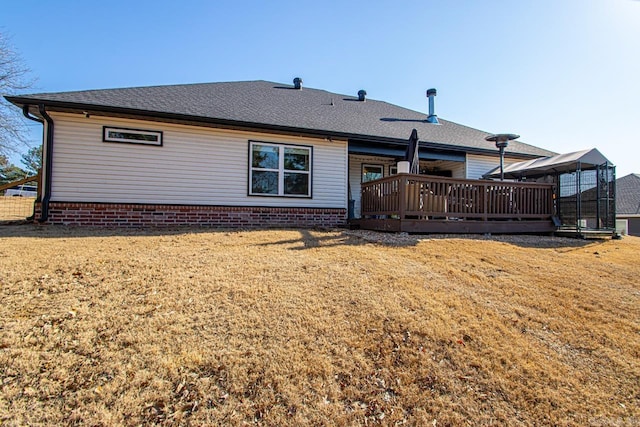 rear view of house with a deck, a yard, and roof with shingles