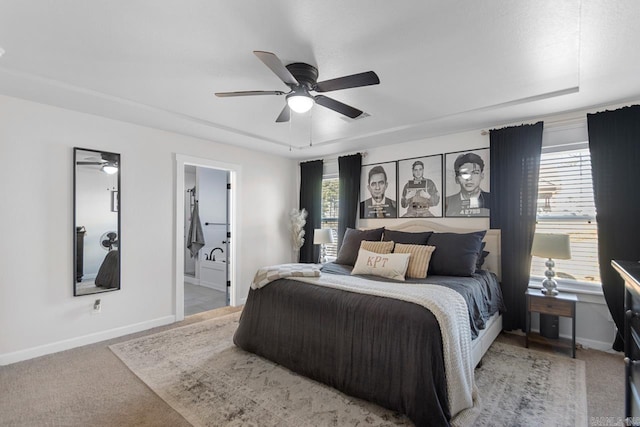 bedroom featuring a raised ceiling, light colored carpet, a ceiling fan, ensuite bath, and baseboards