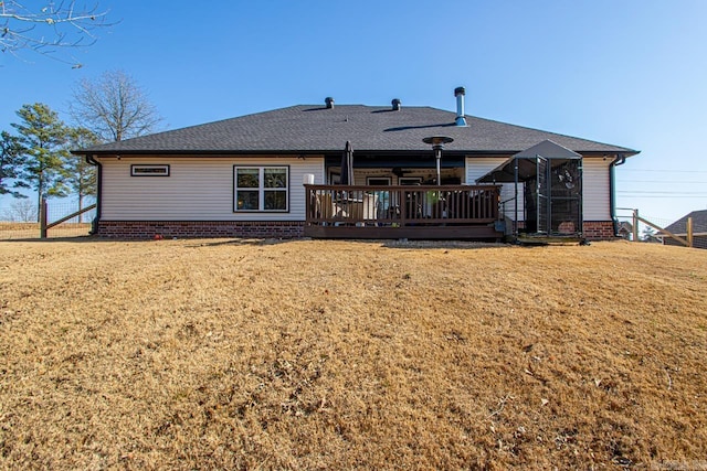 back of house with a deck, roof with shingles, and a lawn