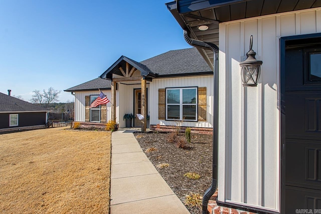 doorway to property featuring board and batten siding, roof with shingles, and a yard