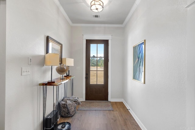 doorway featuring baseboards, visible vents, wood finished floors, and ornamental molding