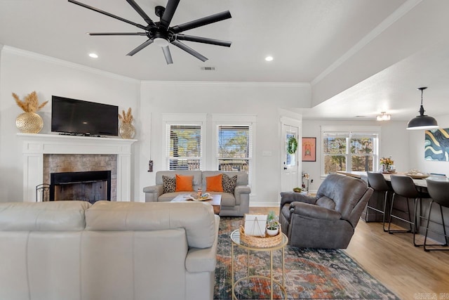 living area featuring crown molding, visible vents, a fireplace, and light wood finished floors