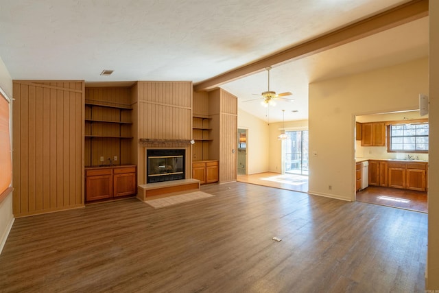 unfurnished living room featuring a large fireplace, visible vents, lofted ceiling with beams, ceiling fan, and wood finished floors