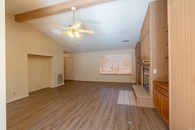 unfurnished living room featuring ceiling fan, a fireplace, wood finished floors, visible vents, and beam ceiling