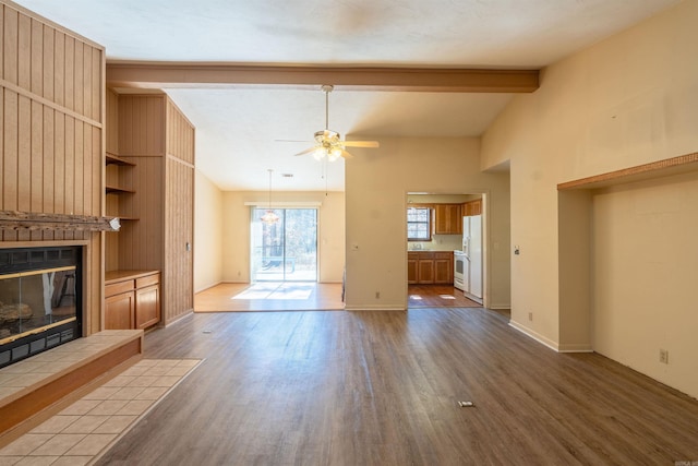 unfurnished living room featuring baseboards, a tiled fireplace, ceiling fan, wood finished floors, and vaulted ceiling with beams