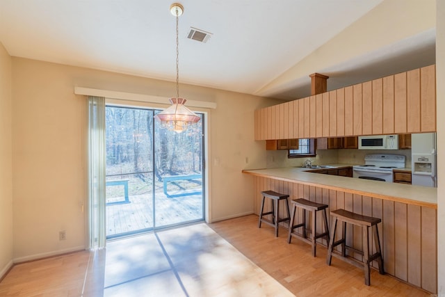 kitchen with a breakfast bar, light countertops, hanging light fixtures, white appliances, and a peninsula