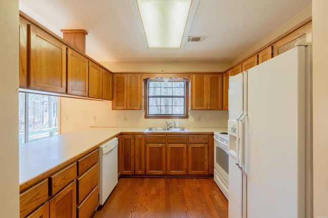 kitchen featuring white appliances, visible vents, brown cabinets, a peninsula, and light countertops