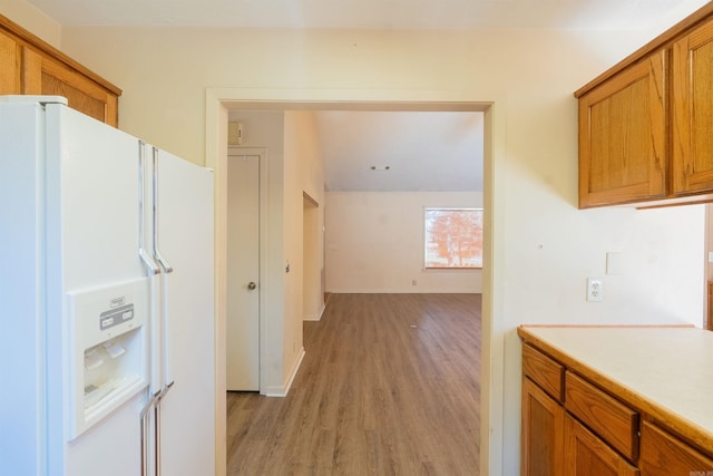 kitchen featuring light wood finished floors, baseboards, brown cabinetry, light countertops, and white fridge with ice dispenser