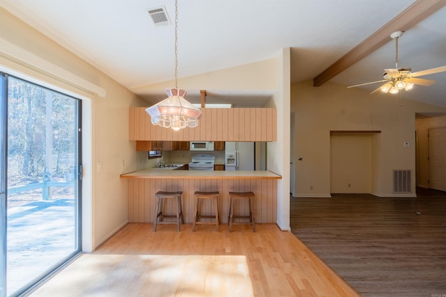 kitchen featuring a breakfast bar area, a peninsula, white appliances, visible vents, and light countertops