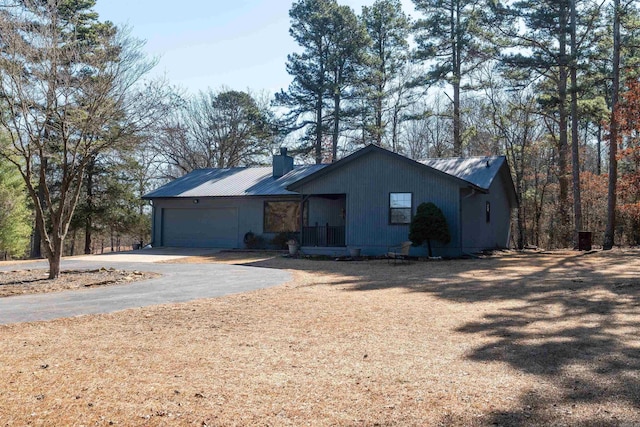 view of front of property with a garage, driveway, metal roof, and a chimney