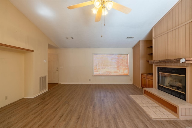 unfurnished living room with vaulted ceiling, light wood finished floors, a tile fireplace, and visible vents