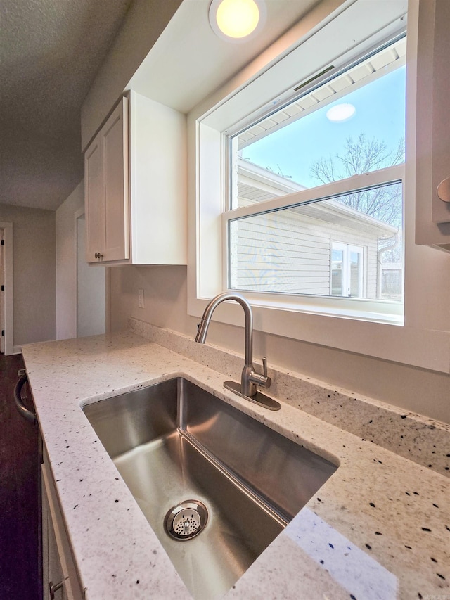 kitchen featuring light stone countertops, white cabinetry, and a sink