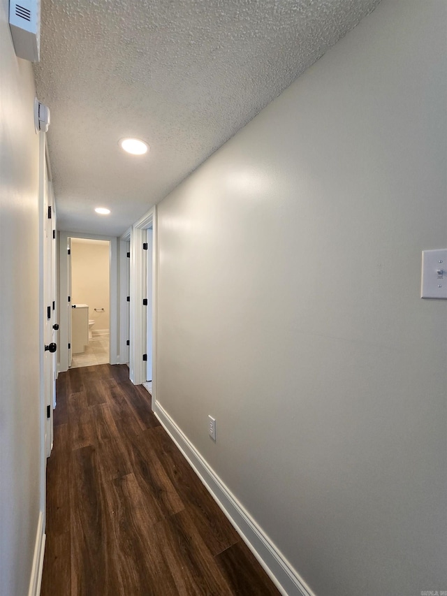 hall featuring dark wood-type flooring, a textured ceiling, and baseboards