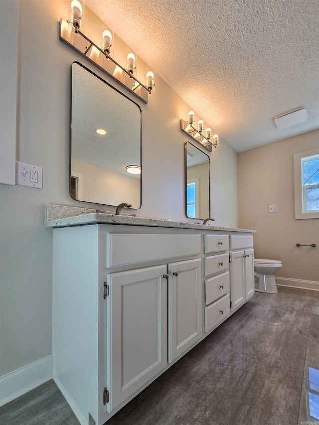 bathroom featuring double vanity, toilet, a sink, a textured ceiling, and baseboards