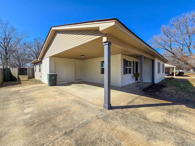 view of side of property featuring driveway, fence, an attached carport, and brick siding