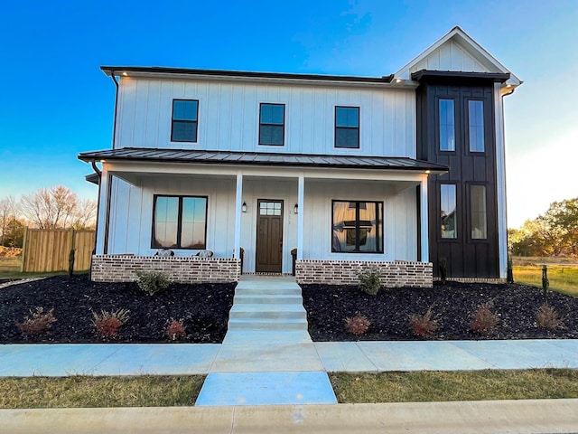 modern inspired farmhouse with brick siding, covered porch, board and batten siding, a standing seam roof, and fence