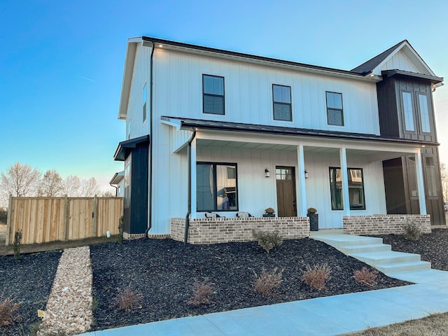 modern inspired farmhouse featuring board and batten siding, covered porch, and fence