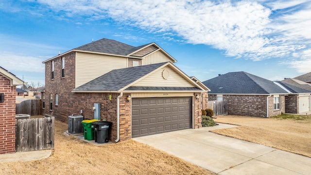 view of front facade with brick siding, concrete driveway, an attached garage, central AC unit, and fence