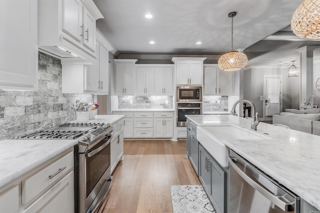 kitchen featuring appliances with stainless steel finishes, white cabinets, a sink, and light wood finished floors