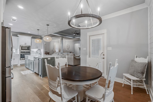 dining room with ornamental molding, light wood finished floors, visible vents, and baseboards