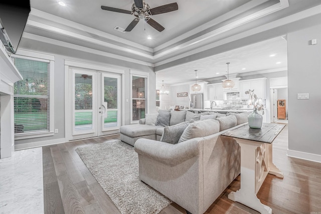 living room with wood finished floors, visible vents, baseboards, ornamental molding, and a raised ceiling