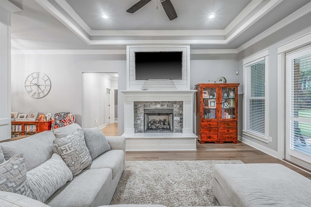 living room featuring ceiling fan, a fireplace, a raised ceiling, and wood finished floors