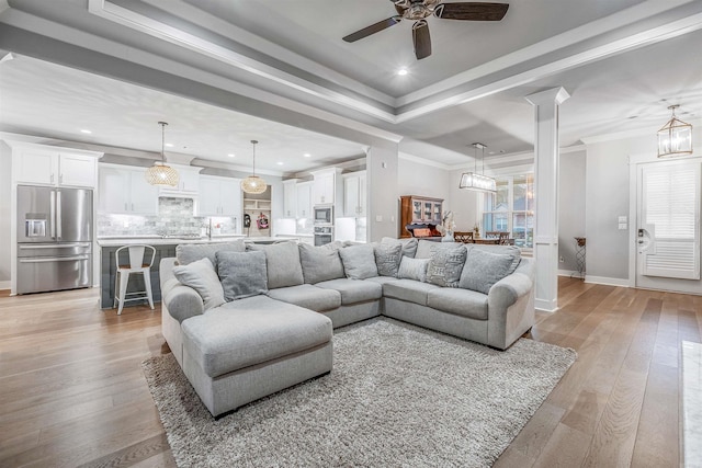 living room featuring light wood-type flooring, a raised ceiling, crown molding, and baseboards