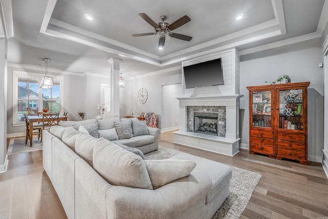 living area with a tray ceiling, a fireplace with raised hearth, crown molding, and light wood-style flooring