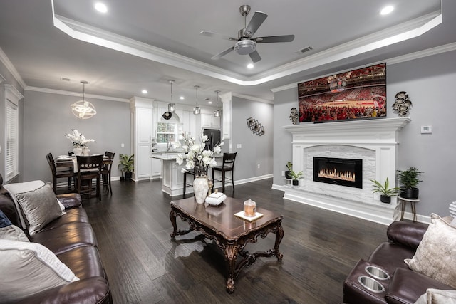 living area with a tray ceiling, dark wood finished floors, visible vents, ornamental molding, and baseboards