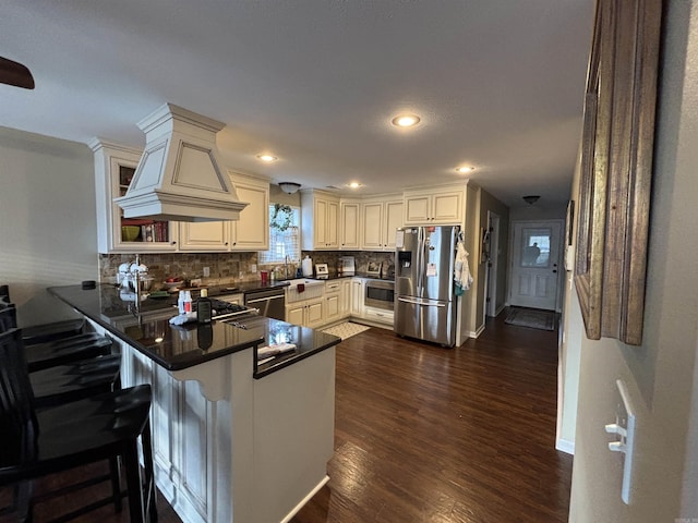 kitchen with stainless steel appliances, tasteful backsplash, dark wood-type flooring, premium range hood, and a peninsula