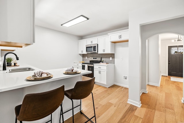 kitchen featuring arched walkways, stainless steel appliances, light wood-style flooring, a sink, and a kitchen breakfast bar