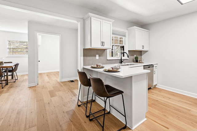 kitchen featuring a sink, white cabinets, dishwasher, light wood finished floors, and a kitchen bar