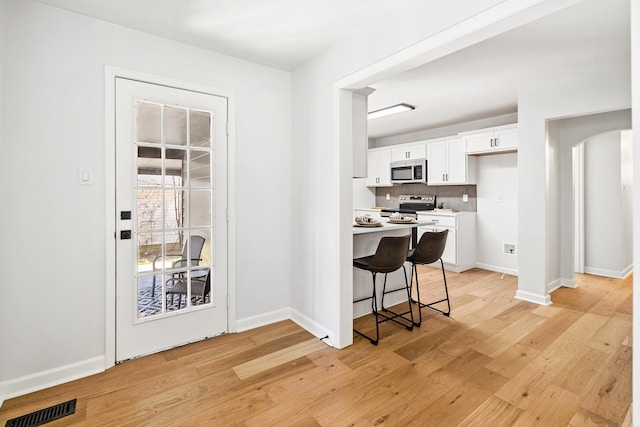 kitchen with arched walkways, light wood finished floors, visible vents, appliances with stainless steel finishes, and white cabinets