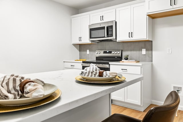 kitchen featuring light wood finished floors, white cabinets, decorative backsplash, light stone countertops, and stainless steel appliances