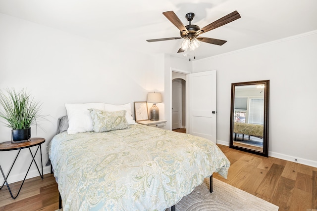 bedroom featuring arched walkways, crown molding, baseboards, and light wood-style floors