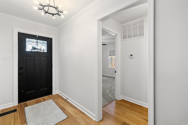 foyer entrance with a notable chandelier, visible vents, light wood-style floors, baseboards, and ornamental molding