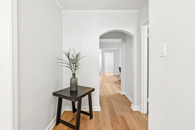 hallway with arched walkways, baseboards, crown molding, and light wood finished floors