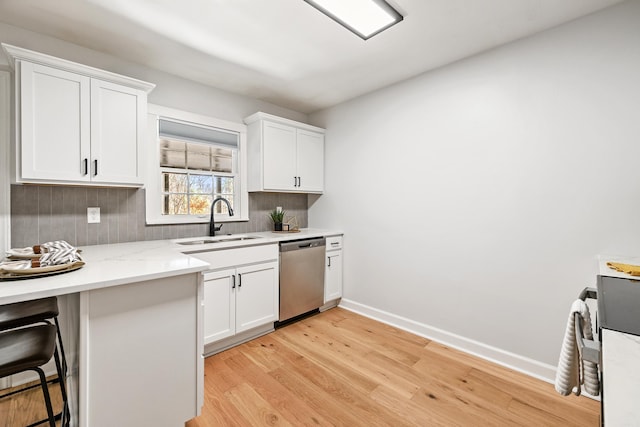 kitchen with baseboards, light wood-style flooring, stainless steel dishwasher, white cabinetry, and a sink