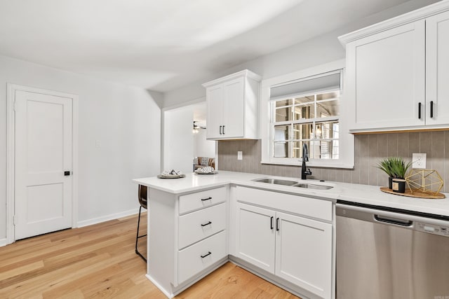 kitchen with light countertops, stainless steel dishwasher, light wood-style floors, a sink, and a peninsula