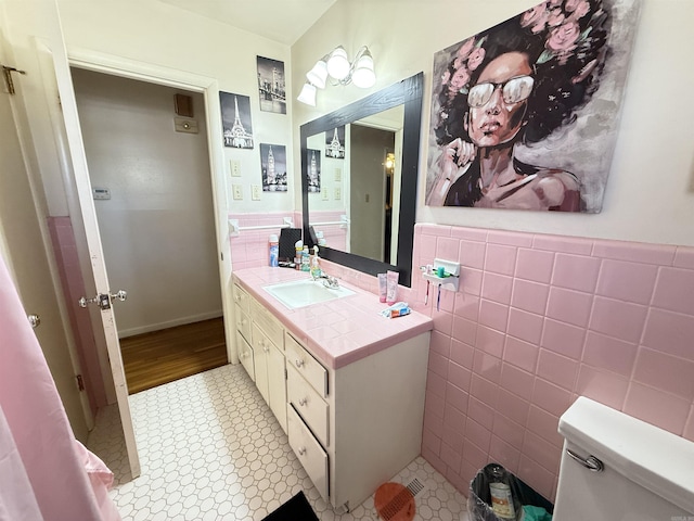 bathroom with toilet, a wainscoted wall, vanity, and tile walls