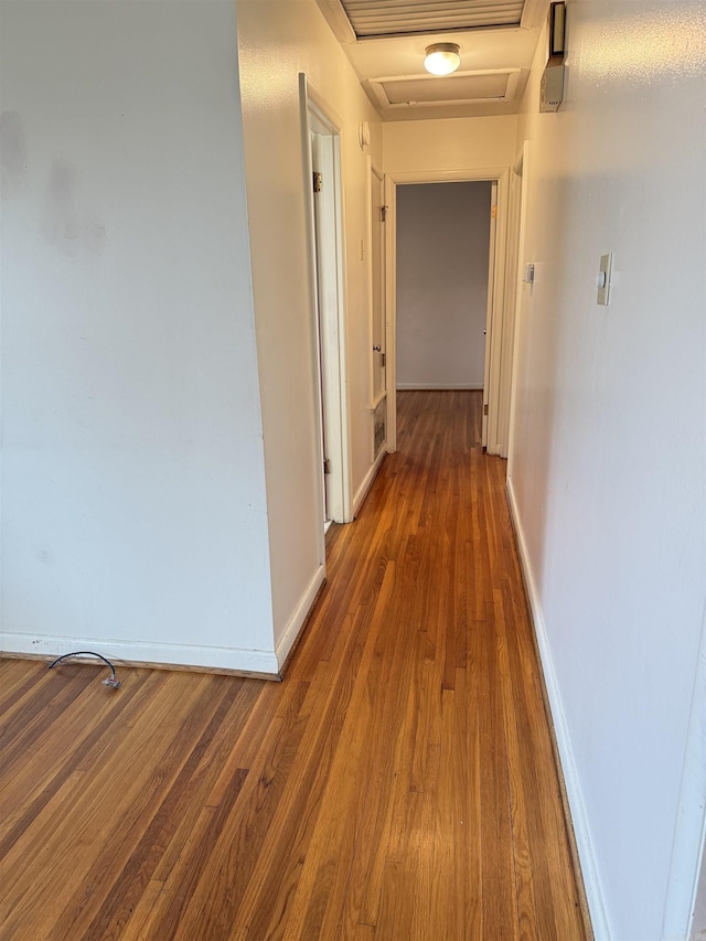 hallway featuring attic access, baseboards, and wood finished floors