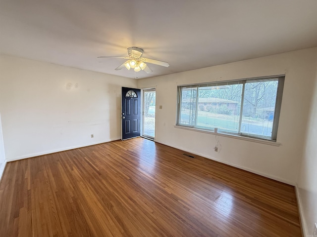 spare room featuring a ceiling fan, visible vents, baseboards, and wood finished floors