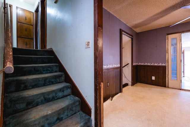 staircase featuring a wainscoted wall, wooden walls, a textured ceiling, and tile patterned floors