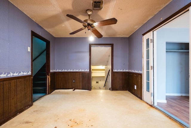 unfurnished bedroom with a wainscoted wall, wood walls, visible vents, and tile patterned floors