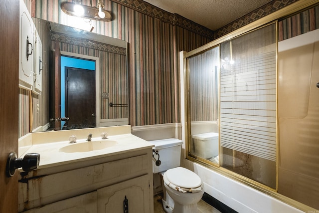 bathroom with a textured ceiling, toilet, shower / bath combination with glass door, vanity, and wallpapered walls