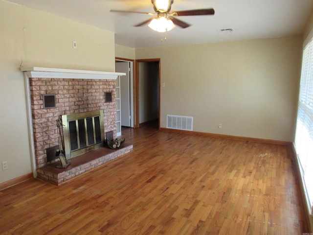 unfurnished living room with a fireplace, wood finished floors, visible vents, and a ceiling fan